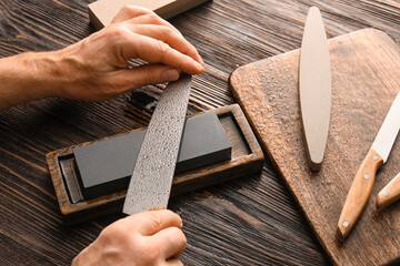 Man sharpening knife on wooden background