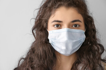 Young woman wearing medical mask on grey background