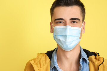 Young man wearing medical mask on color background