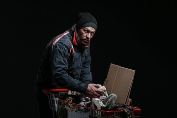 Poor homeless man with donations on dark background