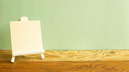 Easel with blank canvas on wooden table. green background