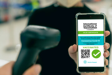asian female show Smartphone displaying a valid digital vaccination certificate passport for COVID-19 in male's hand, public area background. Vaccination, disease immunity passpor