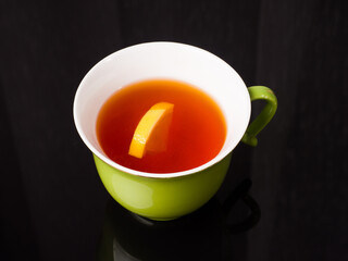 Lemon tea in a green cup on a black glass background. Studio photography