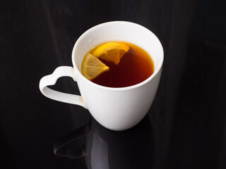 Lemon tea in a white cup on a black glass background. Studio photography