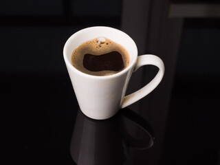 Black coffee in a cup on a black glass background. Studio photography