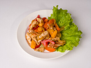 Hot meat salad. Chicken, pepper and persimmon pieces on a white plate. Studio photography