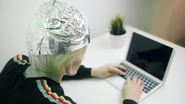 Fearful woman with aluminum hat working on laptop. Protection against 5g and mind reading and control