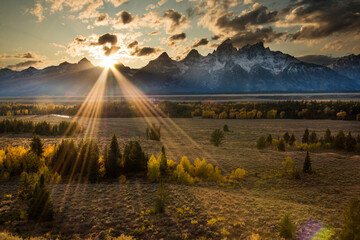 dramatic sunset in the snow capped peaks  of  the Grand Teton Mountain range and vibrant autumn colors of the trees  in Jackson Hole ,Wyoming.