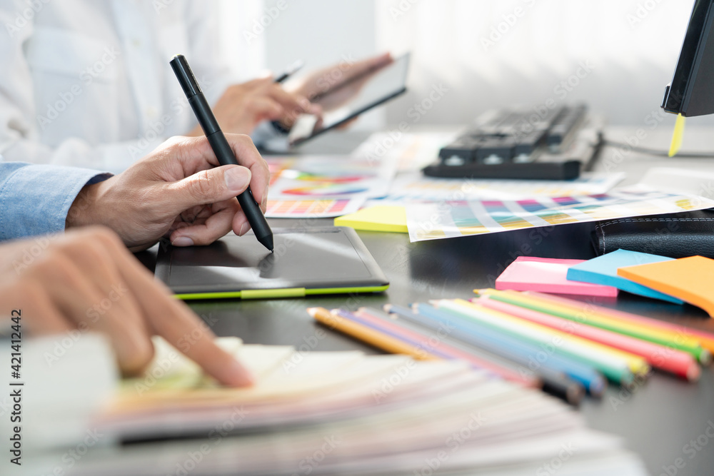 Poster graphic designer or creative working together coloring using graphics tablet and a stylus at desk wi