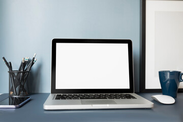 Mock up laptop computer with white screen, mobile phone, coffee up and stationery on dark blue table.