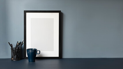 Contemporary workplace with empty frame, coffee cup and copy space on dark blue table.