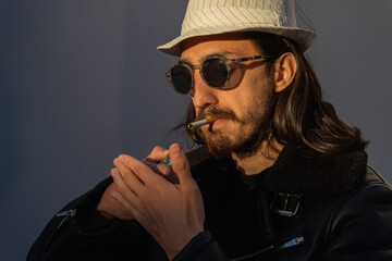 stylish man lighting a cigarette. leather jacket and white hat. anti tobacco.