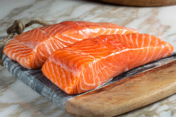 two pieces of raw salmon, on wooden board and marble table