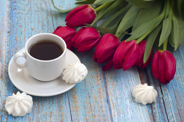 Fototapeta na wymiar bouquet of red tulips, cup of coffee, meringue on blue wooden background