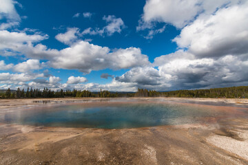 dramatic landscape of a hot spring overcast by large cotton like clouds  in the Midway Geyser basin in Yellowstone in Wyoming.