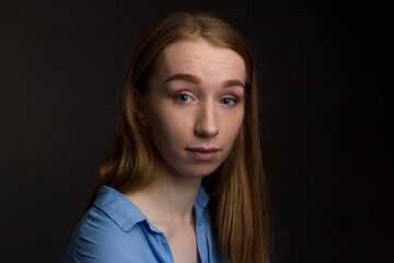 A young woman in a blue blouse, a portrait on a black studio background.