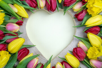 Herz aus Holz umgeben von Blumen (Tulpen und Narzissen). Frühling, Ostern, Muttertag, Geburtstag