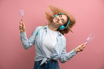 Cheerful young girl with kitchen appliances on a background of a pink wall listens to music. Beautiful woman in headphones dancing.