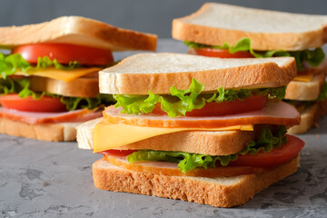 Three tasty sandwiches with ham, salad, cheese and tomatoes on gray background, selective focus, close-up view