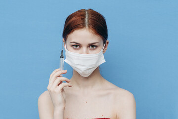 woman with syringe in hand and medical mask injection blue background