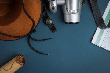 Cowboy hat, camera, compass, geographic map, old paper scroll and seashell on a blue background.