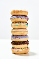 Impressive dessert. Tower of various sweet colorful donuts with sprinkles and glaze isolated over light background