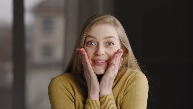Portrait of surprised winner girl blonde caucasian millennial woman feels delight from unexpected good news or gossip closes her mouth with his hands from shock wonder laughing looking at camera
