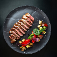 Top view on sliced roast beef with herbs and vegetables on a black plate