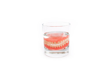A denture in a glass of water. Dental prosthesis care. Full removable plastic denture of the jaws. Two acrylic dentures. Upper and lower jaws with fake teeth. Dentures or false teeth, close-up.