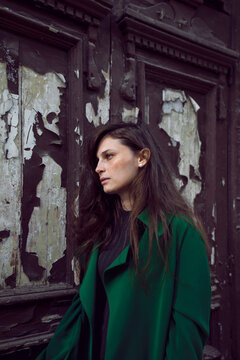 Outside profile portrait of a beautiful young woman in green coat, old door background.