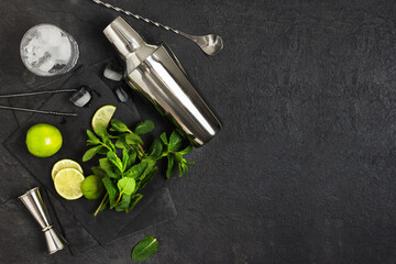 Ingredients and bar utensils for making mojito cocktail with ice cubes, fresh mint and lime on black background.