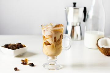 Iced coffee with coconut milk in a tall glass on white wooden table. Cold refreshment summer coffee...