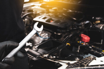The Mechanic's hand holds a wrench behind himself with a sunlight and car engine blurred on background