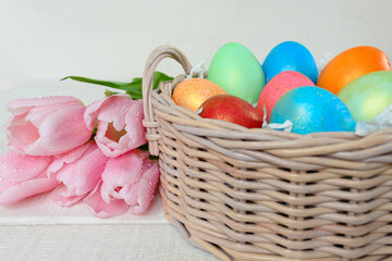 Painted chicken eggs in a wicker basket and pink tulips on a white table. Easter concept Handmade, creativity with children for decoration on easter
