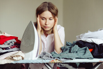 Sad young woman ironing clothing at home