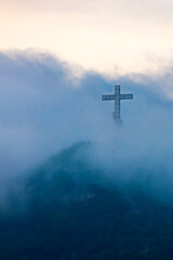 A single cross stands on a mountain engulfed in white clouds
