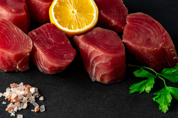 Fresh raw tuna steak with parsley and lemon. Raw tuna fillet. Seafood on black slate close up.