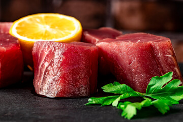 Fresh raw tuna steak with parsley and lemon. Raw tuna fillet. Seafood on black slate on a brick...