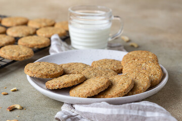 Healthy oatmeal cookies with cereals, seeds and nuts with a cup of milk on concrete background. Diet vegan cookies.