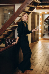 A beautiful stylish blonde woman in a black outfit relaxes with a glass of wine in her hands. Soft selective focus, defocus, art noise