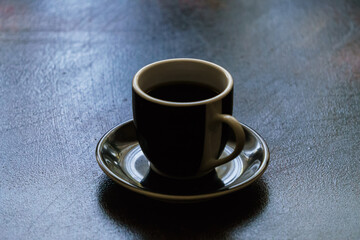 Black ceramic earthenware coffee cup on a saucer on a dark clean table.