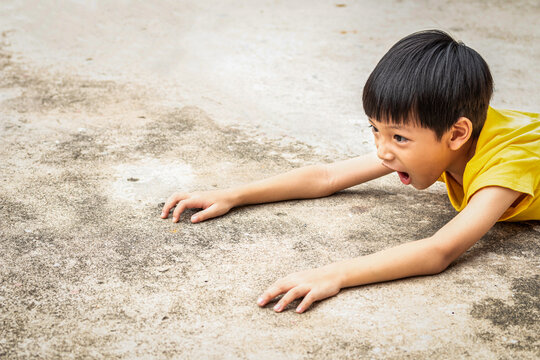 The boy falls to the cement floor. Making a very shocked face. The Asian child fell to the ground because he ran carelessly. The kid was stumbling on a rock while walking.