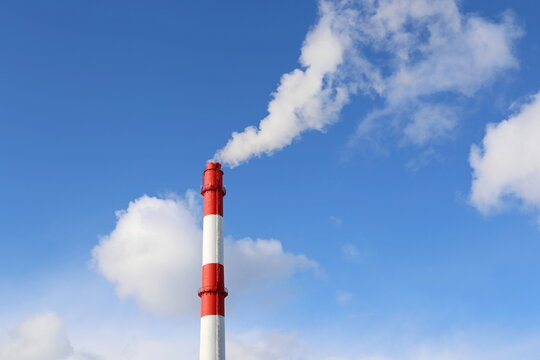 Factory chimney on blue sky and clouds background with white smoke. Concept of steam plant, air pollution, heating season