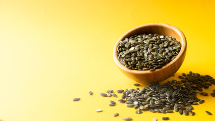 Pumpkin seed or pepita in wooden bowl on yellow background. Modern ingredients background. Copy space