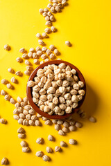 Uncooked chickpea beans on ceramic bowl on yellow background. This legume high in vegetal protein and perfect for vegetarian diet.