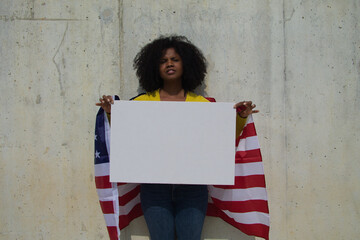 africa-american woman holds a white banner in her hands and united states flag over her shoulder....