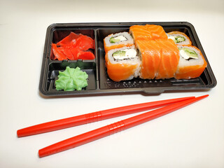 Delicious sushi rolls are served in plastic packaging on an isolated white table background.
