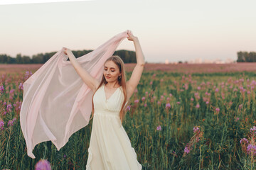 a happy girl with a white scarf walks through a flower meadow. Love and spring blooming