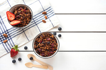 Home-made baked granola in two bowls, with berries, almonds, napkin and eco-friendly spoons. White rustic background, copy space. 