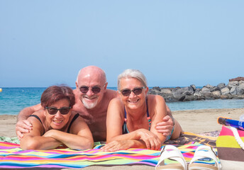 Fototapeta premium Cheerful group of three people lying on the sand sunbathing, enjoying the beach vacation - horizon over the water